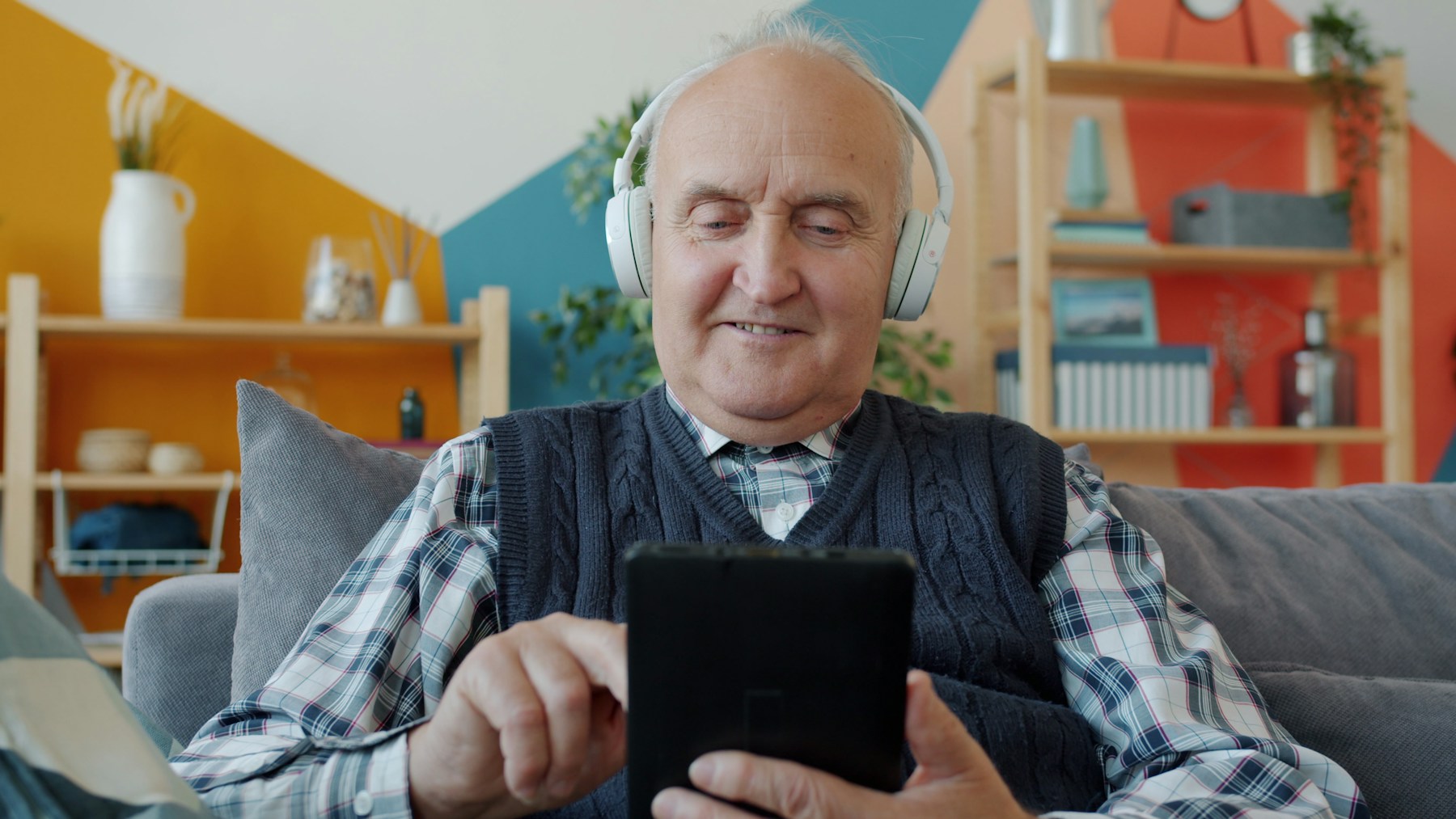An older man using a tablet at home on the sofa.