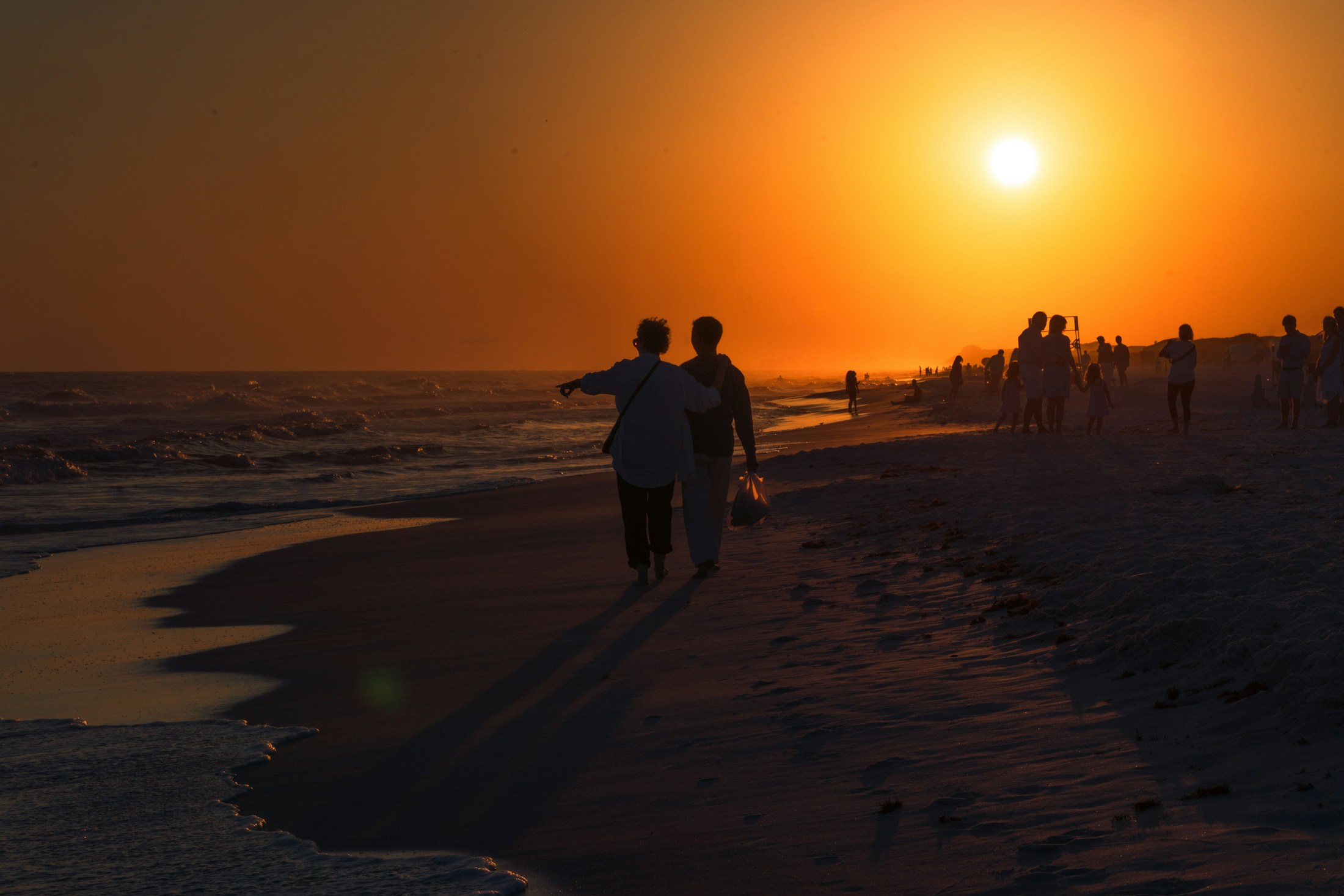 Two people walking together along a shoreline in the late afternoon.